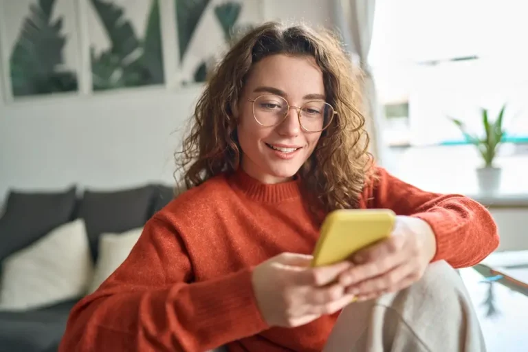 Jeune femme souriante portant des lunettes tenant un smartphone à l'aide de la technologie moderne du téléphone portable